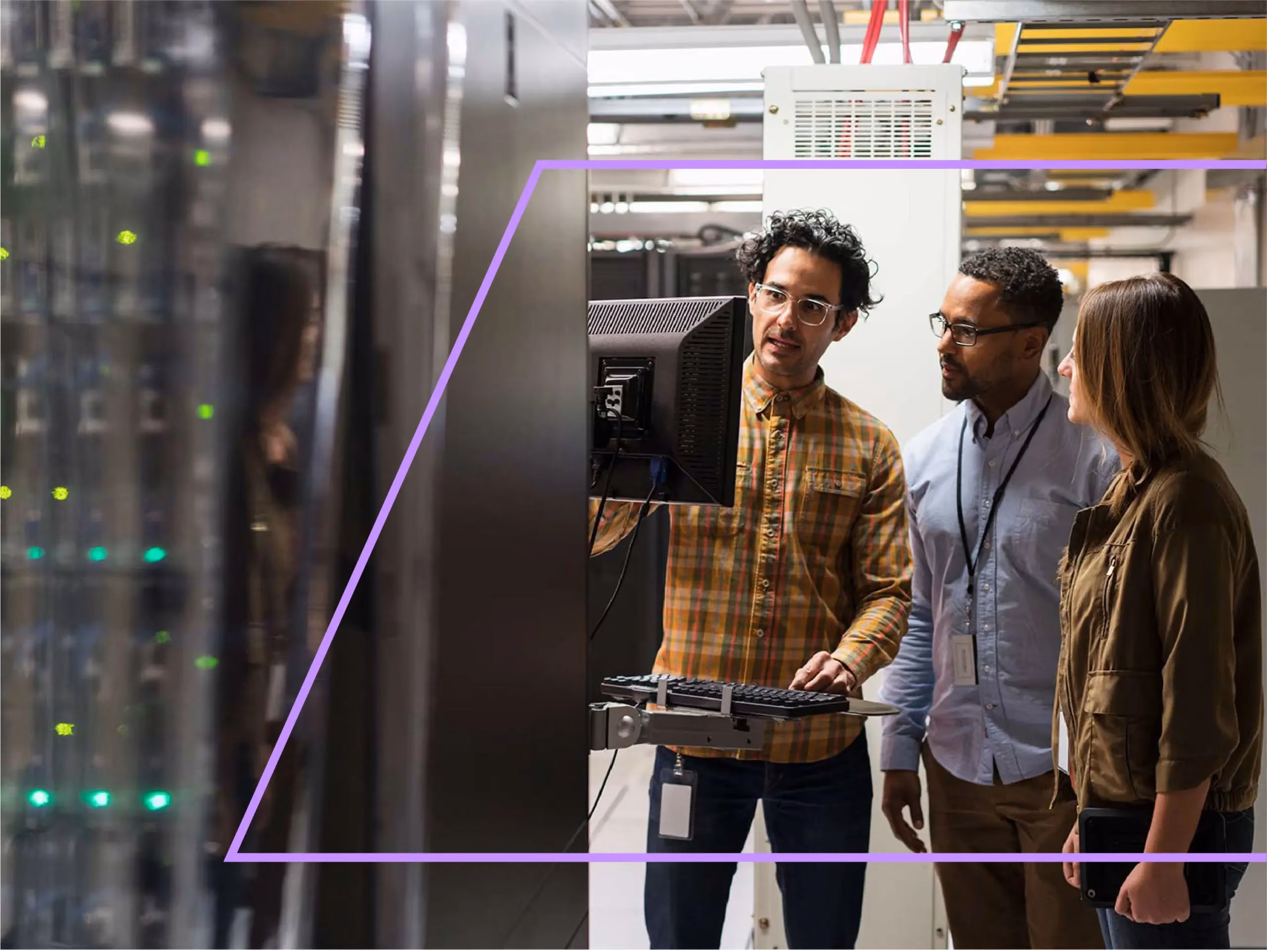 Three IT professionals discuss information on a computer monitor in a server room.