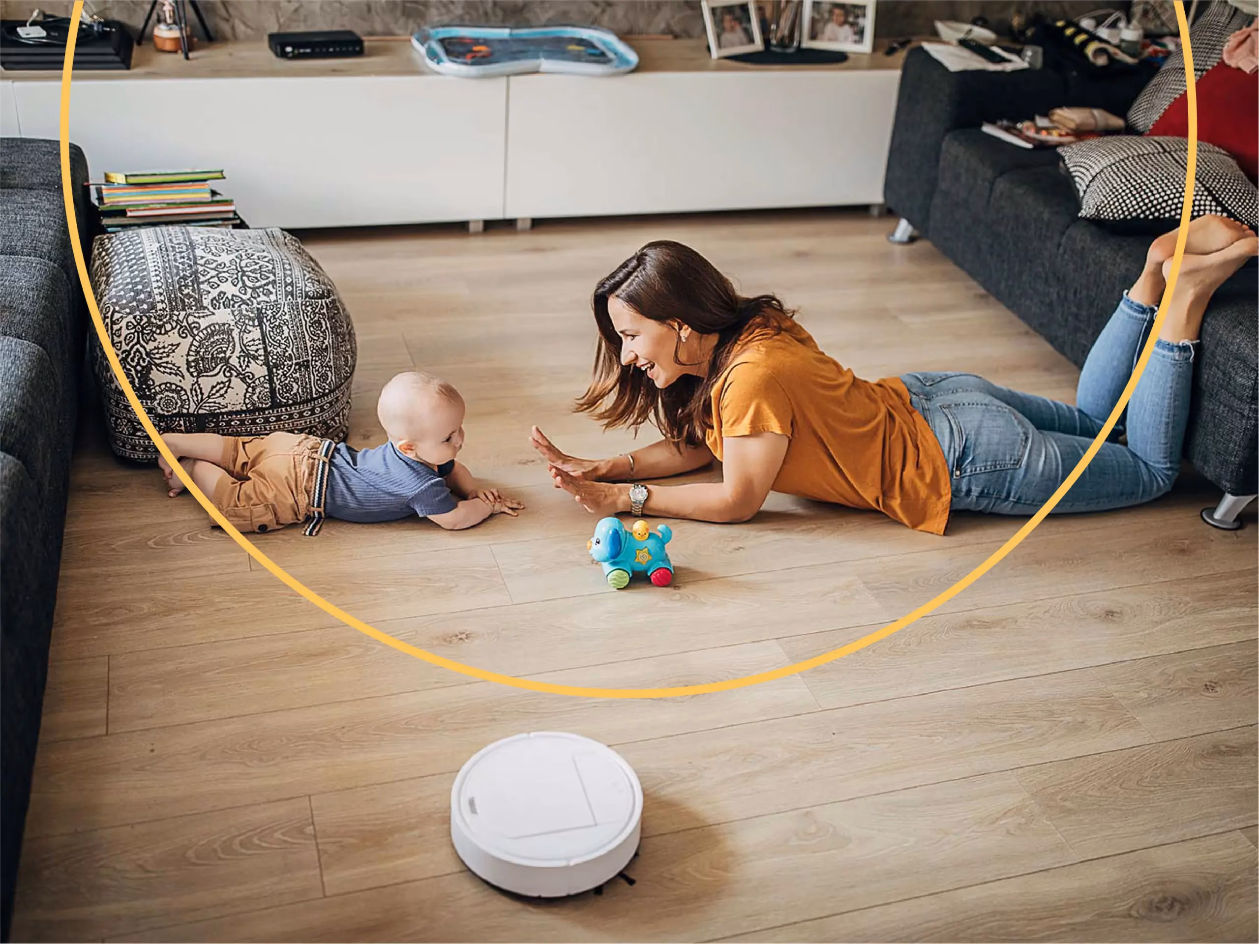 A mother and baby play on the floor near a toy dog while a white robot vacuum cleans nearby.
