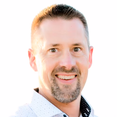 Headshot of a smiling man with short hair and a beard, wearing a white patterned collared shirt.
