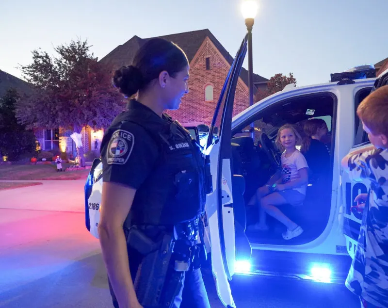 Two police officers and a K9 dog with three smiling boys sitting on grass in a neighborhood.