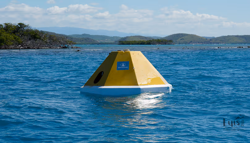 Yellow and white buoy floating on blue water with distant green islands and cloudy sky.