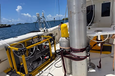 Scientific equipment secured on a boat deck with ocean and partly cloudy sky in the background.