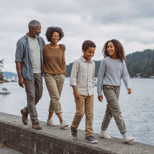 Two adults and two children walking and laughing along a waterfront on a cloudy day.