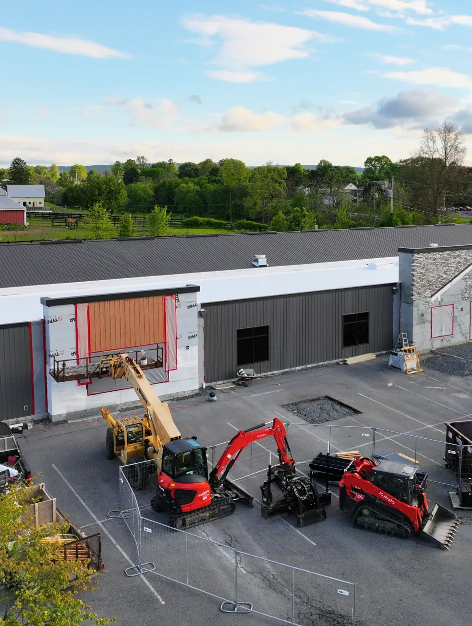 A construction site with three pieces of heavy machinery parked near a gray building.
