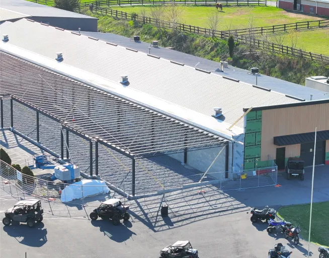 A large building under construction with exposed steel framework, construction materials, vehicles, and equipment visible around the site.