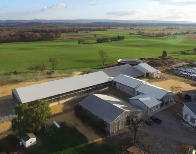 Aerial view of a farm with several large buildings surrounded by green fields and distant trees.