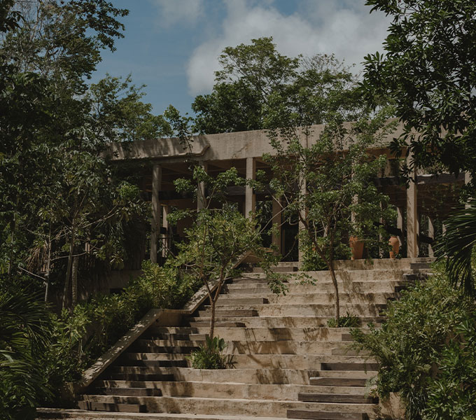A captivating view of the ocean sunset, with a vegetation-covered cliff in the foreground, rock formations, and the restaurant of La Valise Mazunte Hotel.