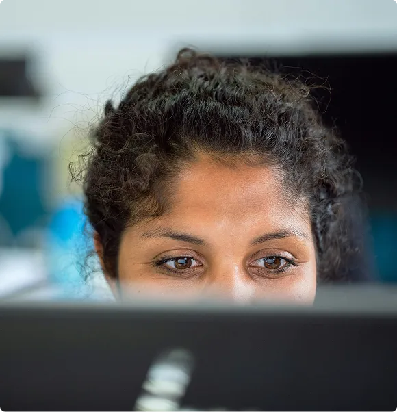 Young person with curly hair focused on a laptop screen in a blurred indoor setting.