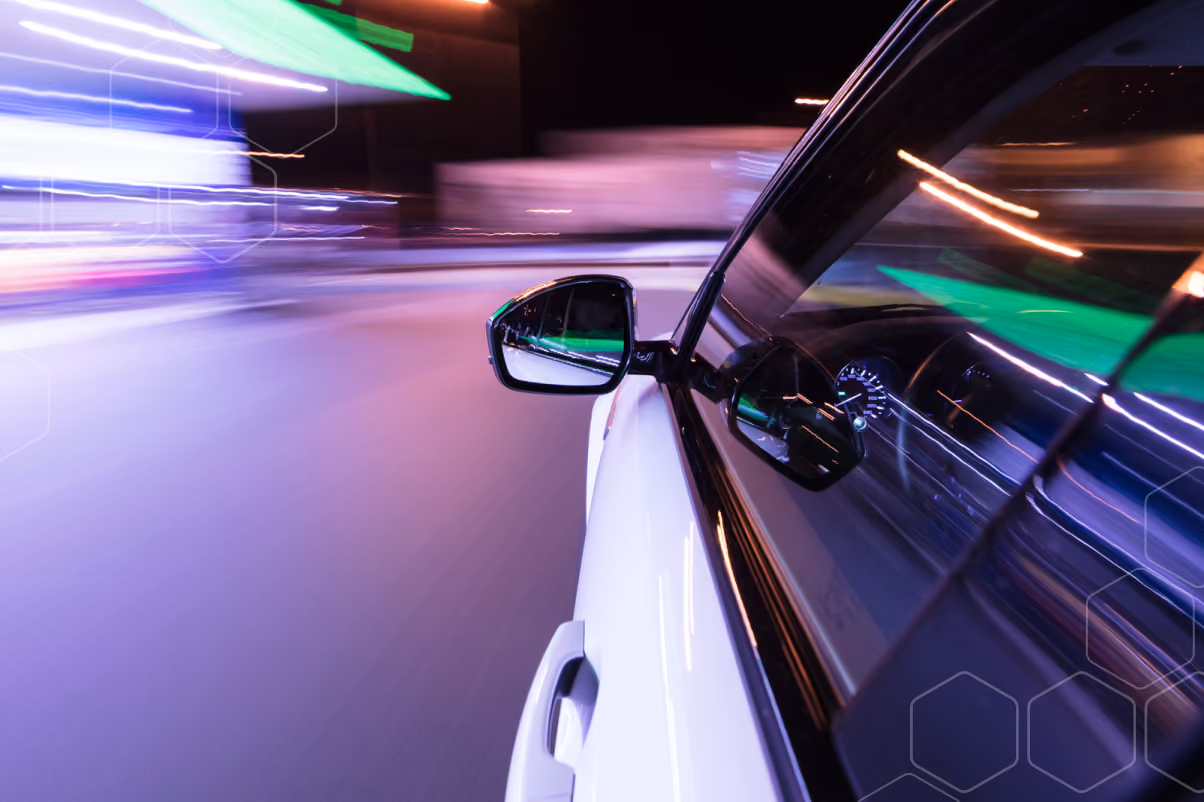 View from a moving white car's side showing blurred city lights and speed at night.
