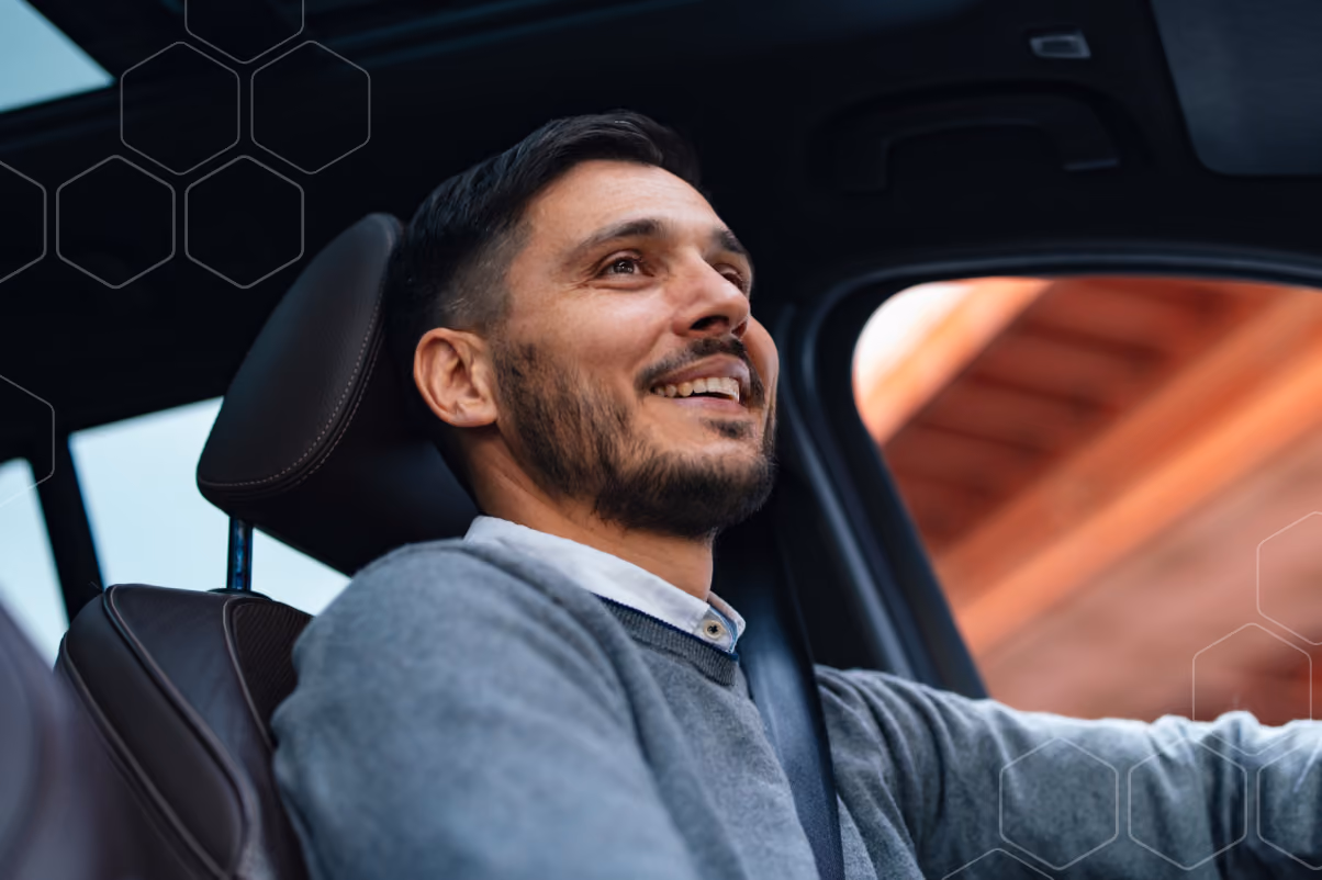 Smiling man driving a car wearing a gray sweater and seatbelt.
