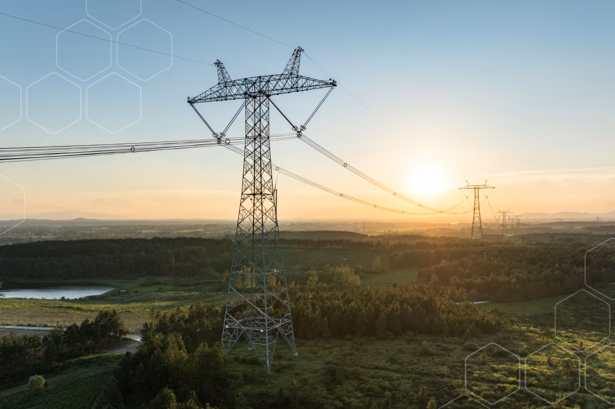 High voltage power lines on tall steel towers stretching over green fields at sunset.