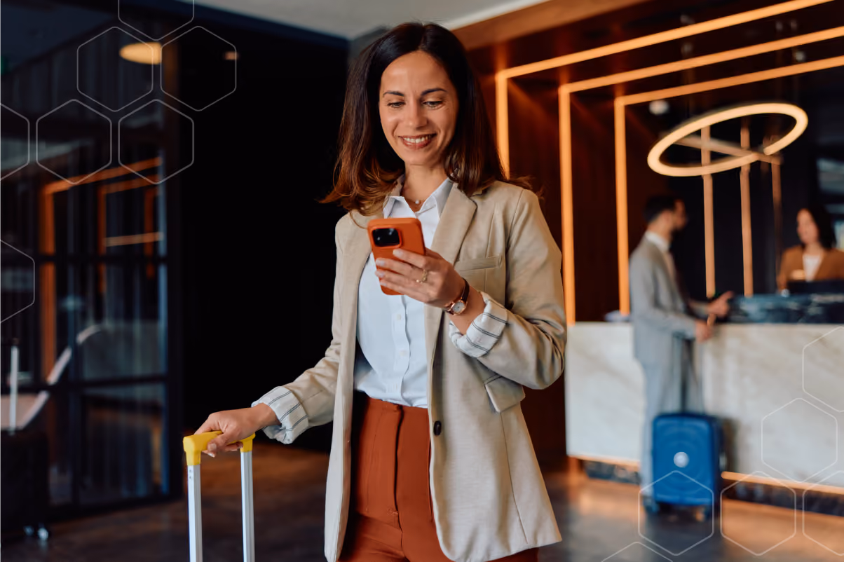 Smiling woman holding a suitcase and looking at her phone in a modern hotel lobby.