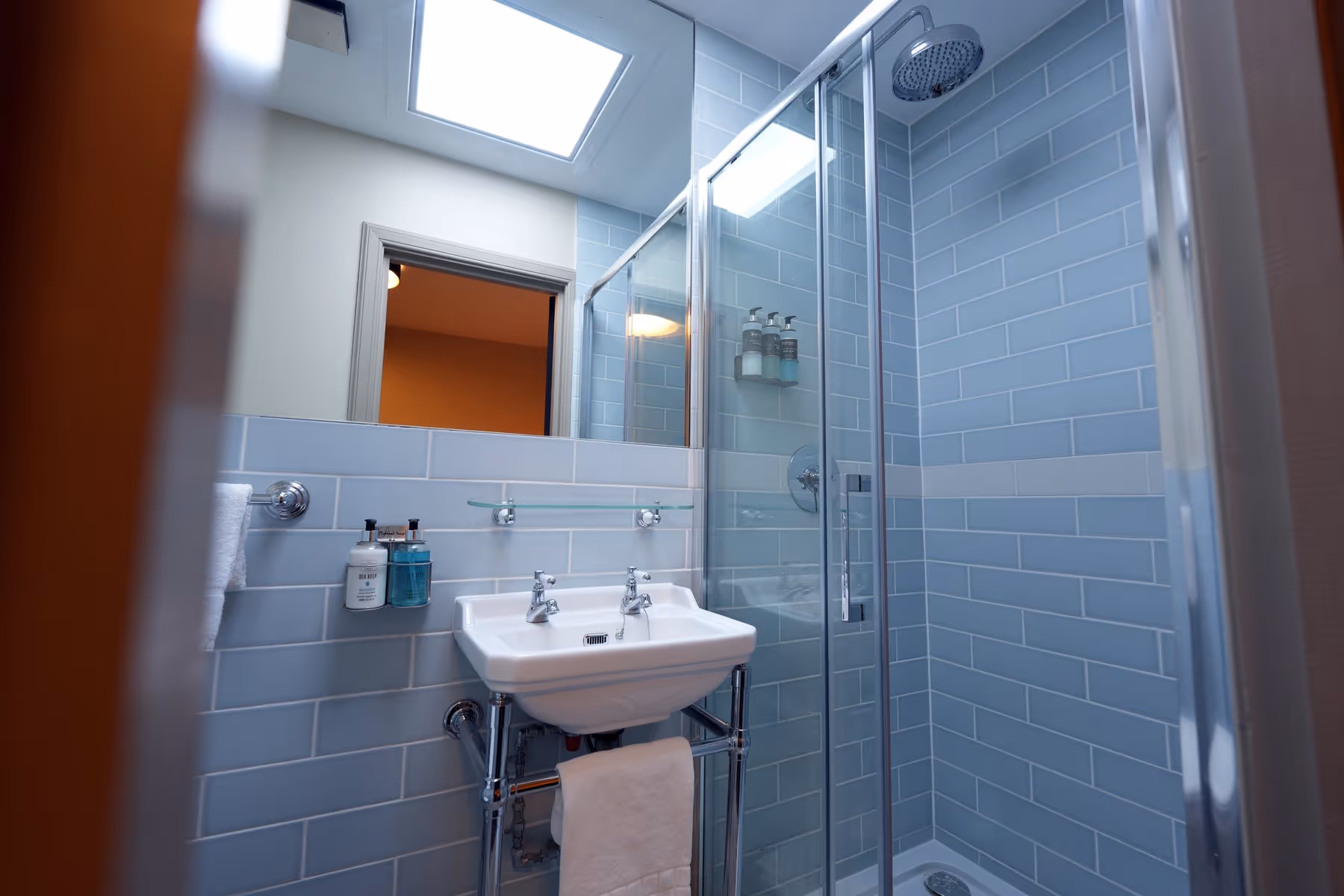 King Room bathroom at Riva Helensburgh — teal-tiled shower enclosure with overhead rainfall head, white basin with chrome taps, and Highland Soap toiletries.