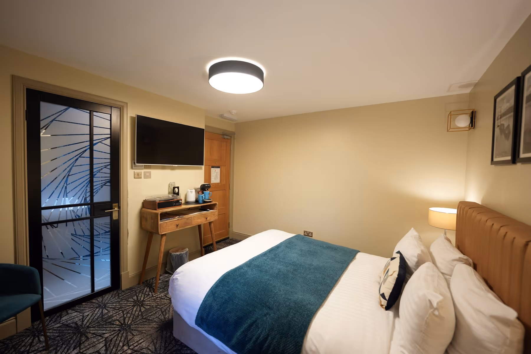 Double Room at Riva Helensburgh — close-up of the double bed with white linen, decorative cushions, and a warm bedside lamp on a wooden nightstand.
