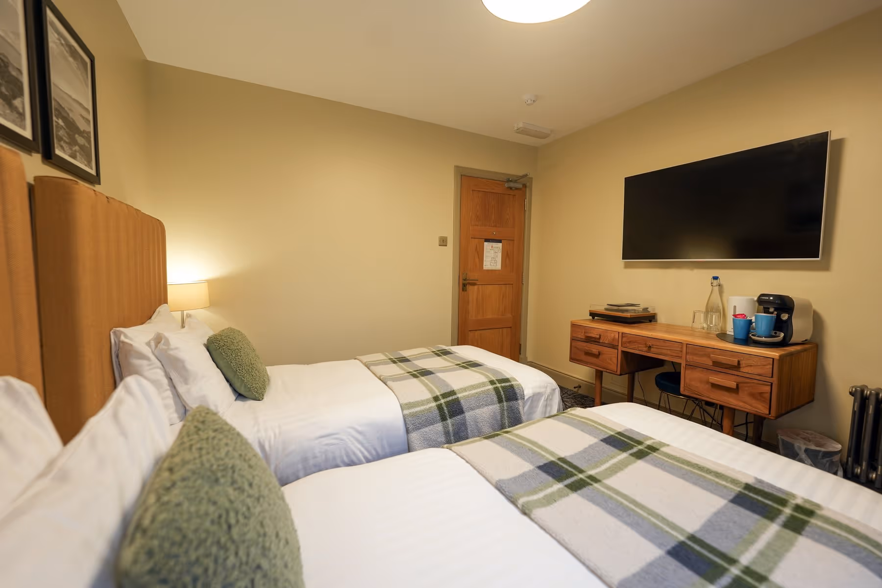 Twin Room at Riva Helensburgh — close-up of the twin beds with white linen and green accent cushions, with Scottish landscape prints above.