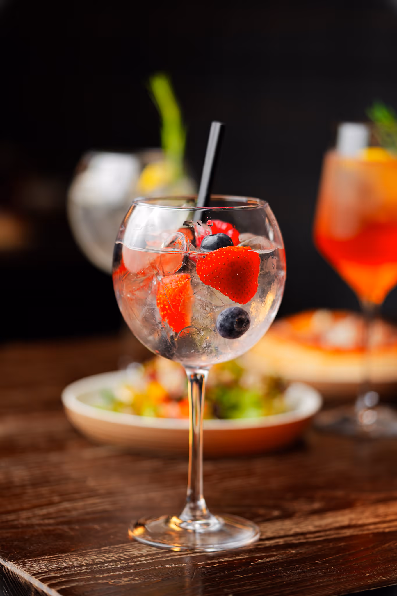 Gin and tonic cocktail garnished with strawberries and blueberries at Santé Bistro, served in a balloon glass with two other drinks visible in the background.