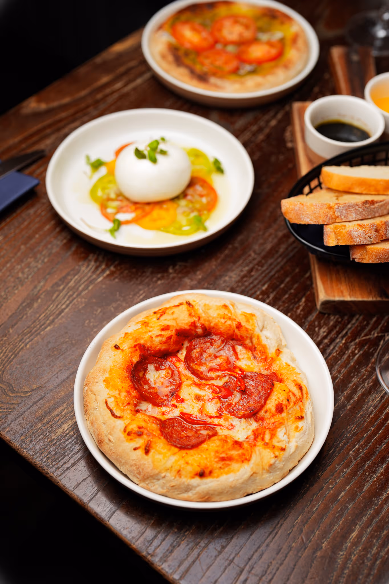 Selection of dishes at Santé Bistro including a pepperoni flatbread, burrata with tomatoes and herbs, and a tomato bruschetta, served on a dark wooden table.