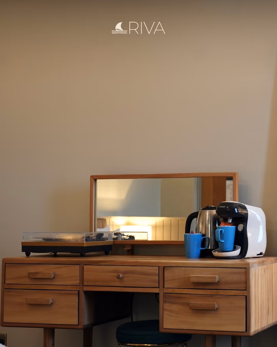 Wooden desk with a mirror, a turntable, a coffee machine, kettle, and two blue mugs.