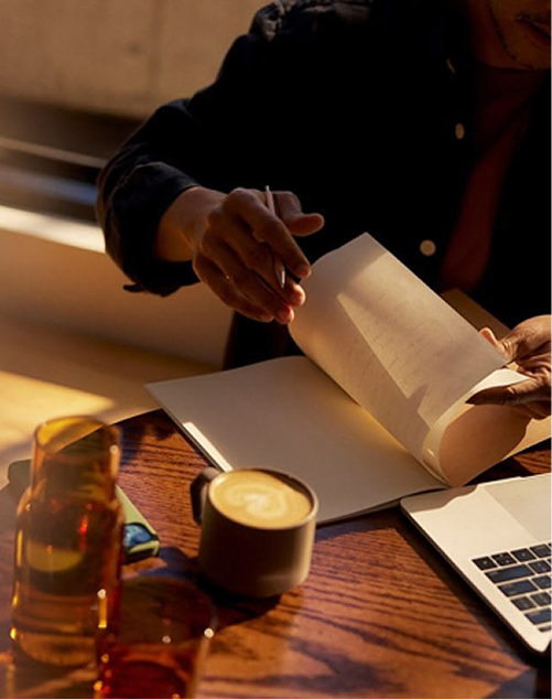 Person turning pages of a notebook beside a coffee