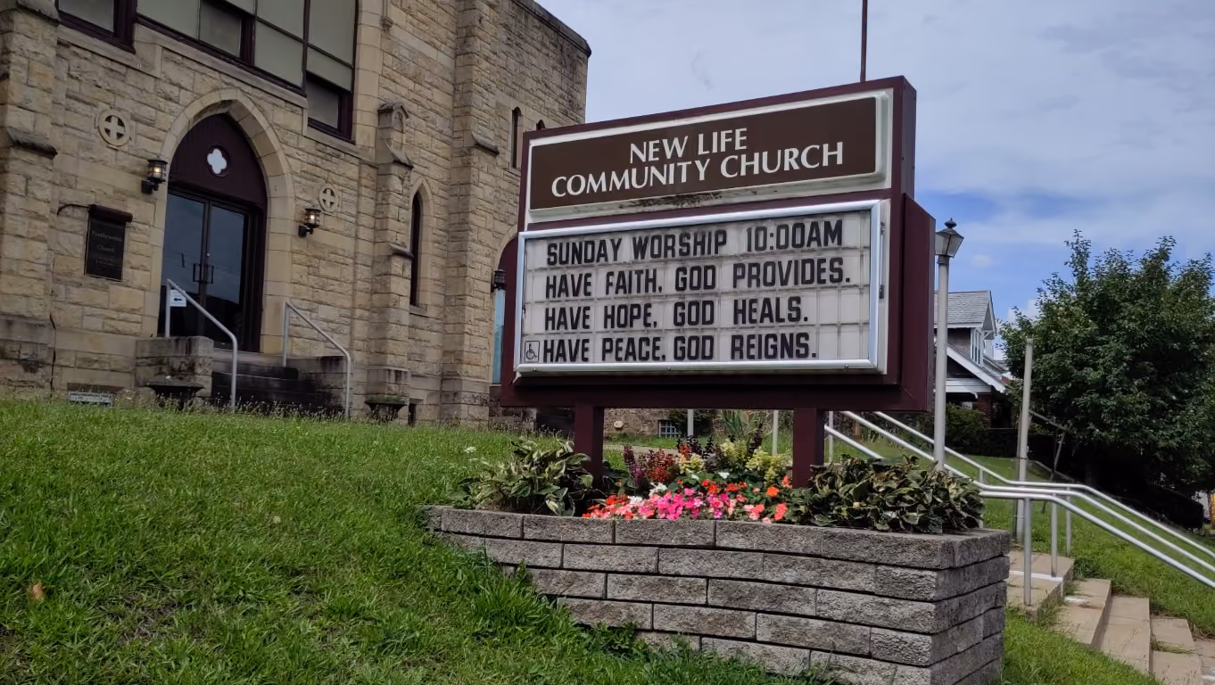 The sign in front of New Life Community Church reads "Sunday Worship 10:00 AM. Have faith, God provides. Have hope, God heals. Have peace, God reigns."