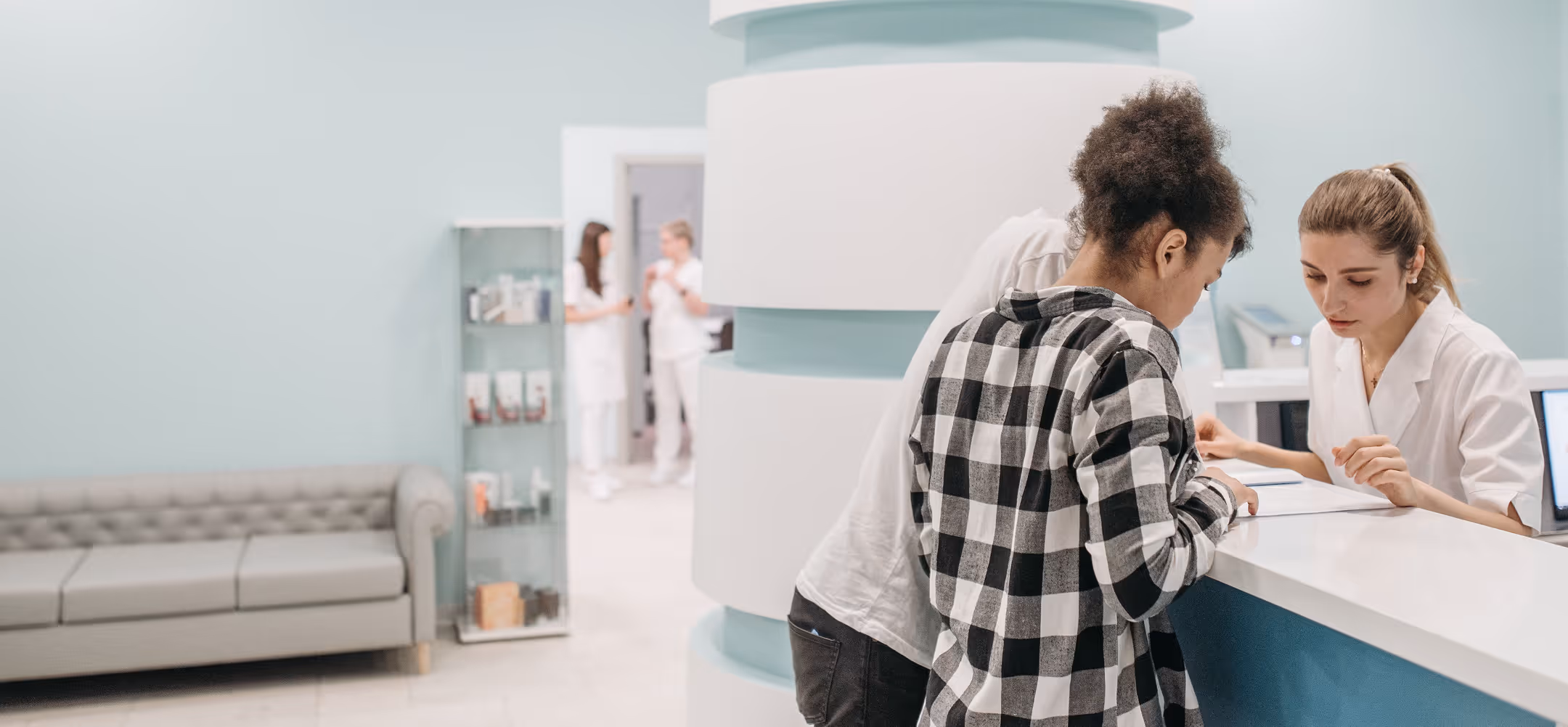 Two patients talking to a receptionist at a modern clinic's front desk with medical staff in background.
