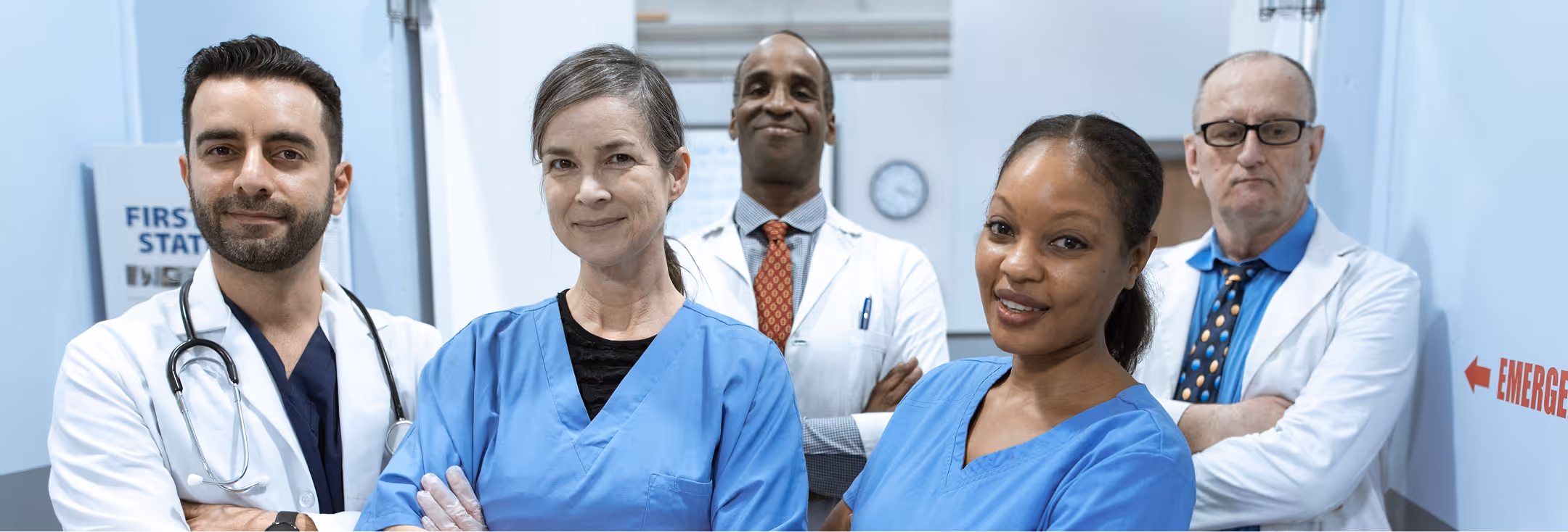 Diverse group of four doctors and one nurse standing confidently in a hospital hallway.
