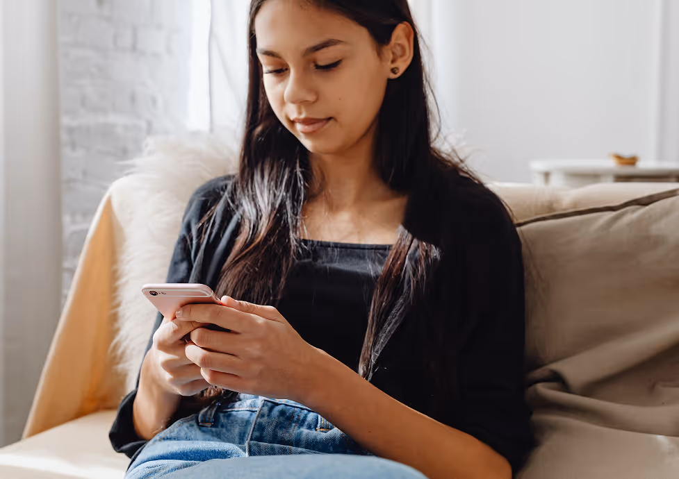 Young woman sitting on a couch looking at her smartphone in a bright room.
