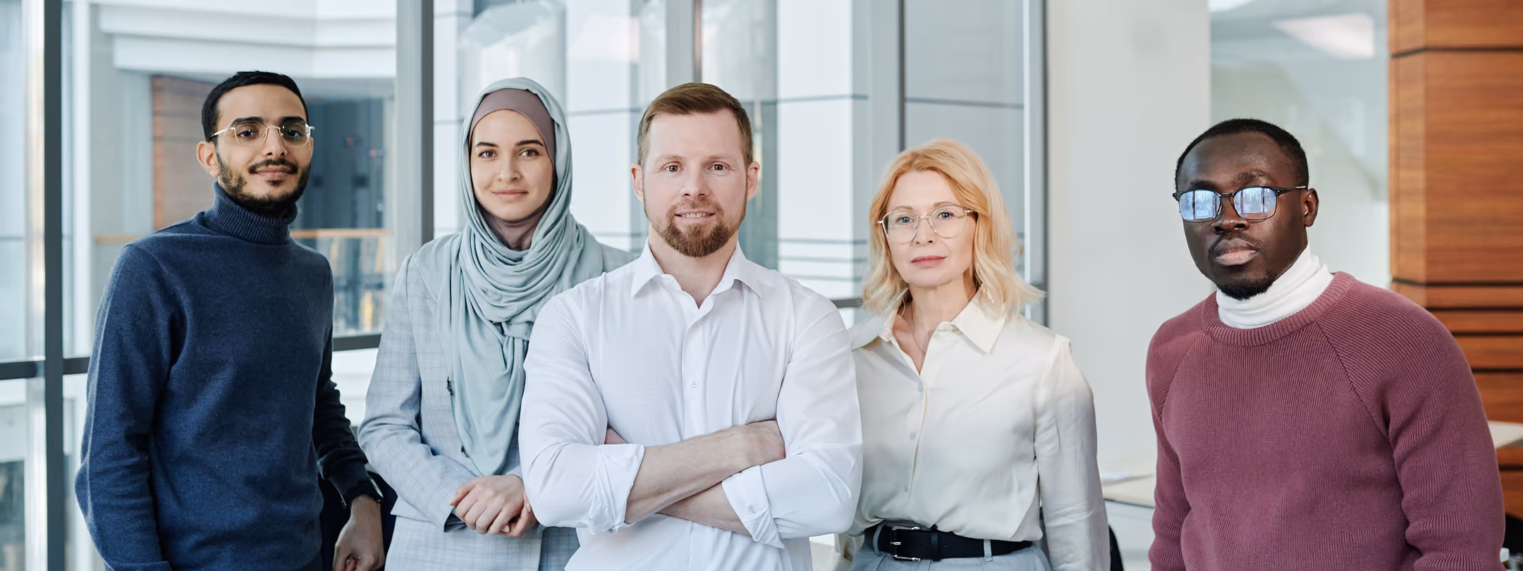 Five diverse professionals standing indoors, facing the camera, with confident expressions.