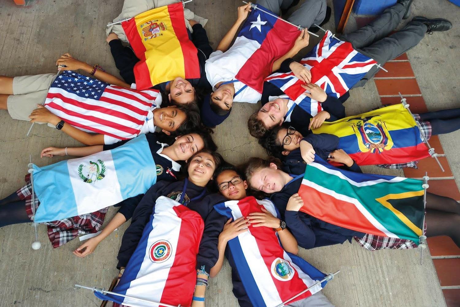 A group of students lying on the ground in a circle holding flags of different countries.