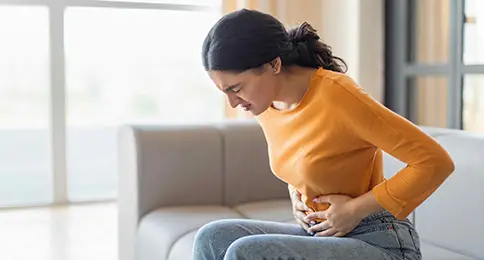 Woman experiencing abdominal discomfort and GI symptoms while seated at home, highlighting the importance of evaluation and treatment from the best GI doctor in Los Angeles, CA for digestive health and gastrointestinal conditions.
