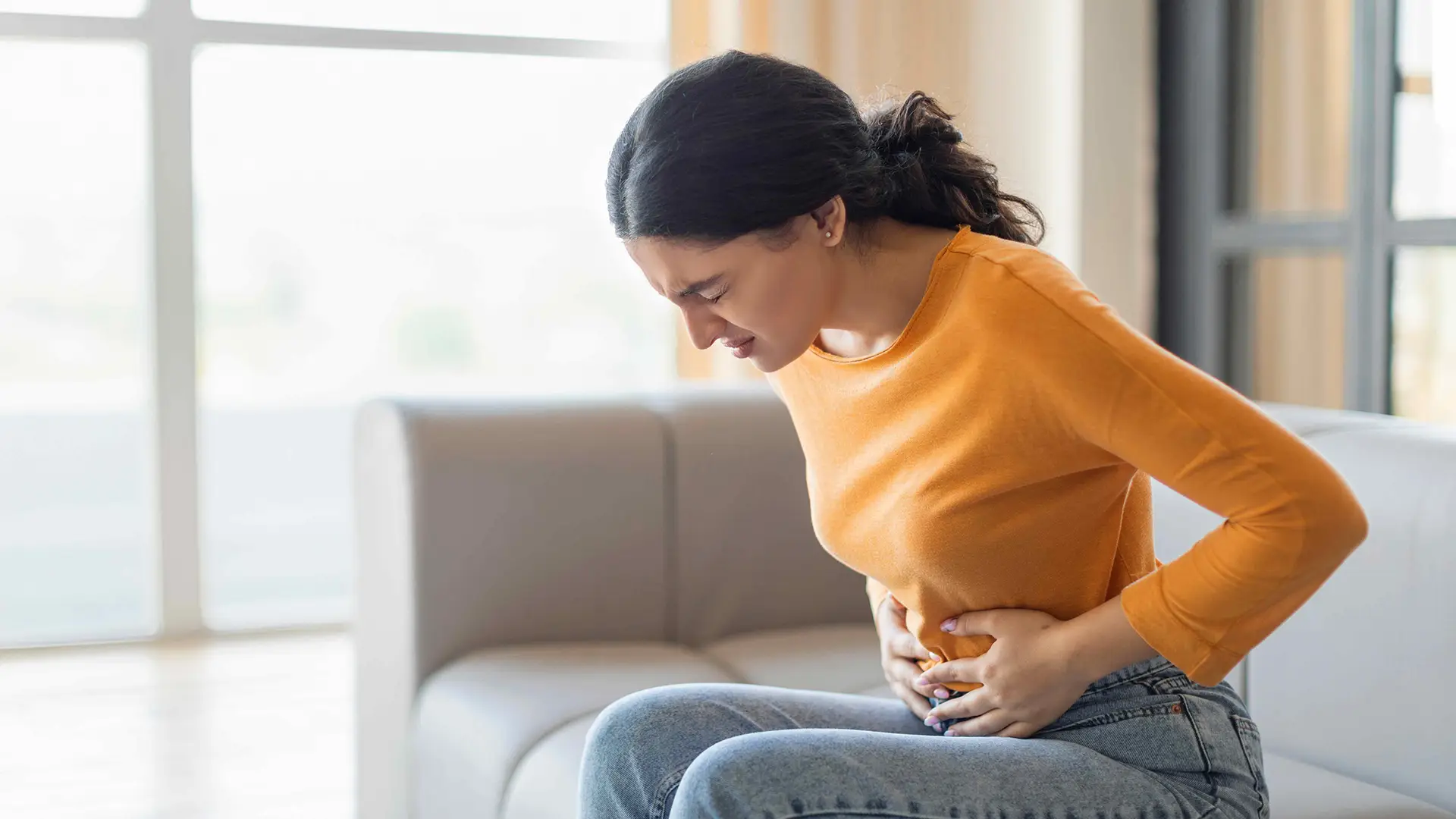 Woman experiencing abdominal discomfort and GI symptoms while seated at home, highlighting the importance of evaluation and treatment from the best GI doctor in Los Angeles, CA for digestive health and gastrointestinal conditions.