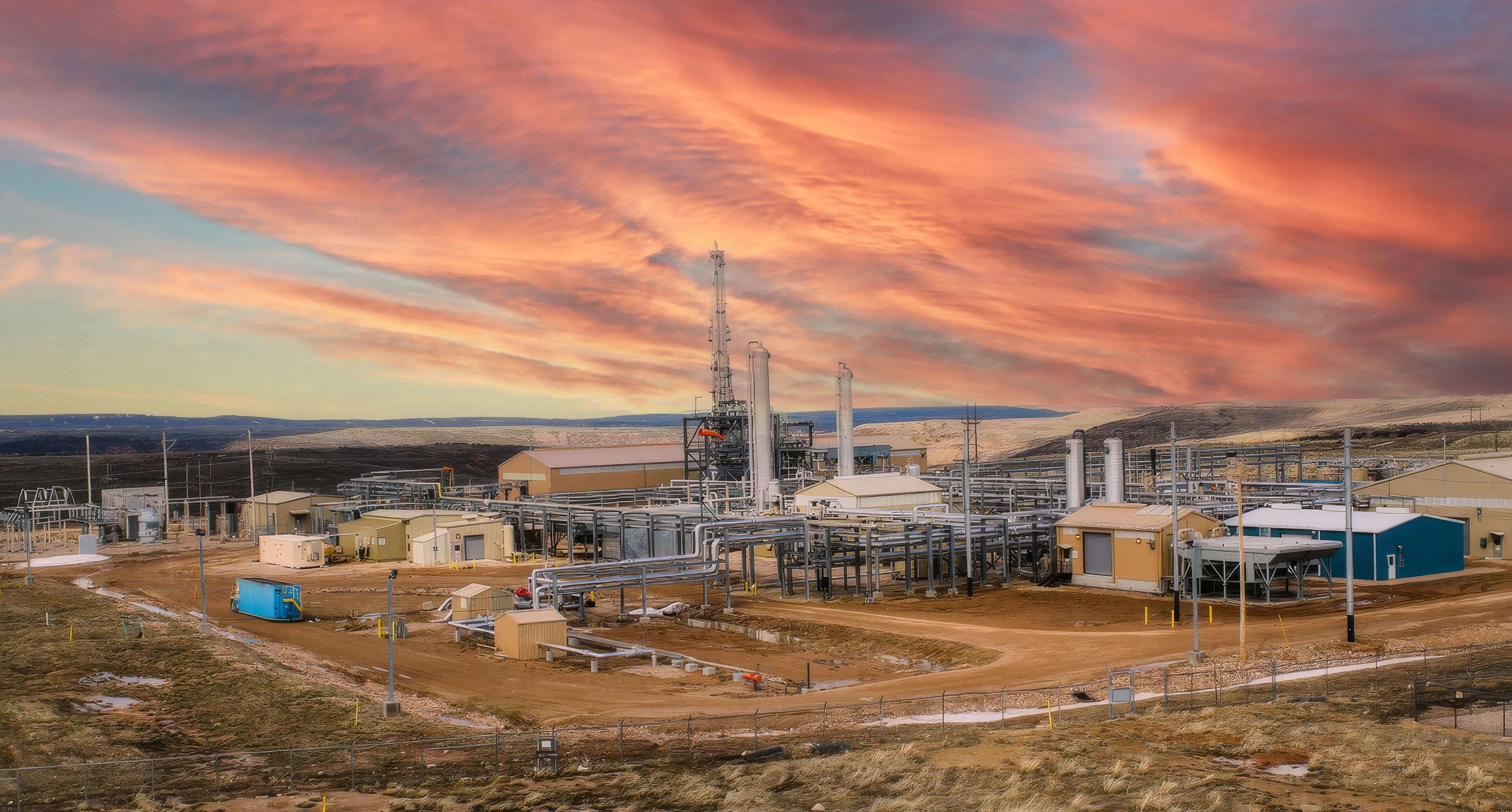 Industrial plant with pipes, buildings, and towers under a vibrant orange and purple sunset sky.