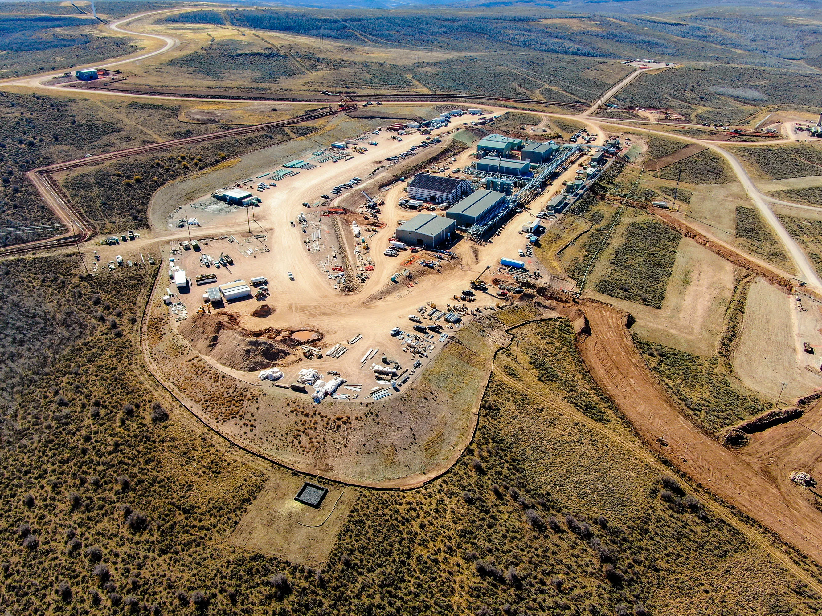 Aerial view of an industrial construction site surrounded by dry grassy terrain and winding roads.