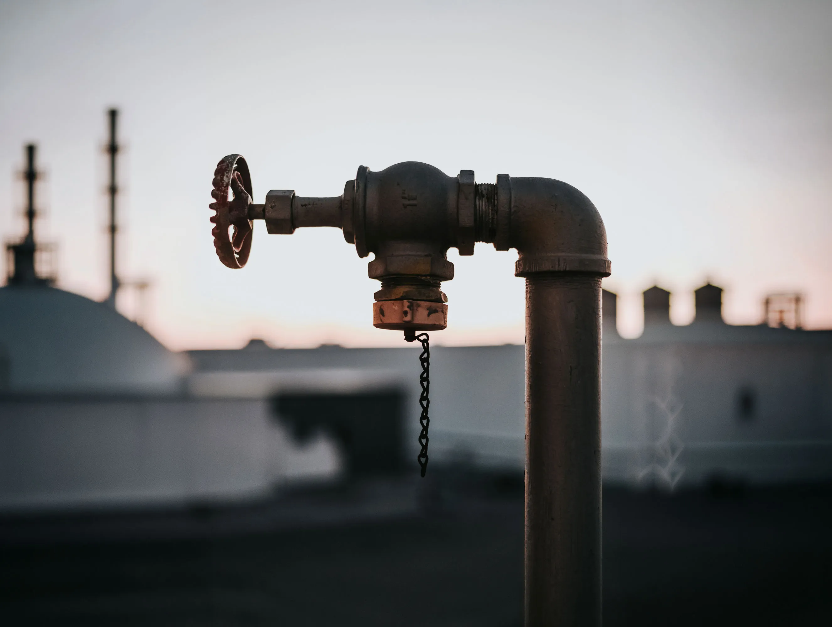 Close-up of a weathered outdoor metal pipe valve with a chain hanging down at dusk.