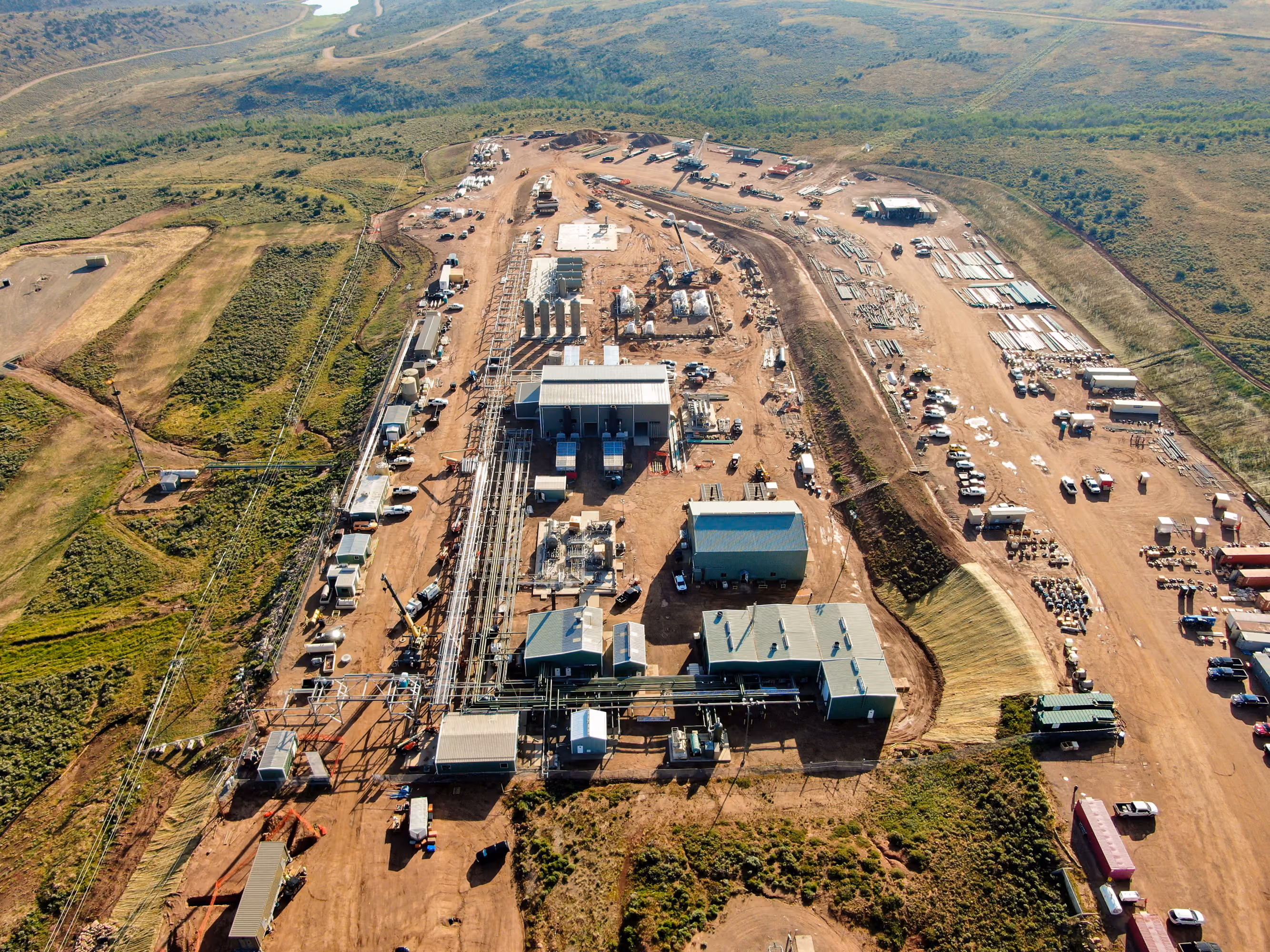 Aerial view of an industrial site with multiple buildings, equipment, and vehicles surrounded by greenery.