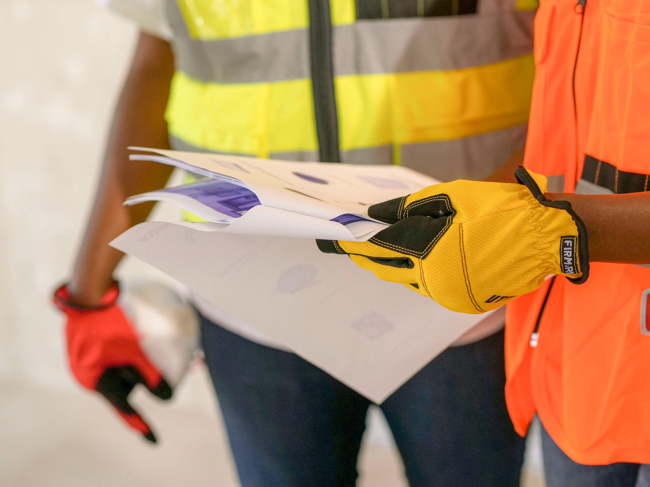 Close-up of two construction workers in safety vests reviewing blueprint documents on site.