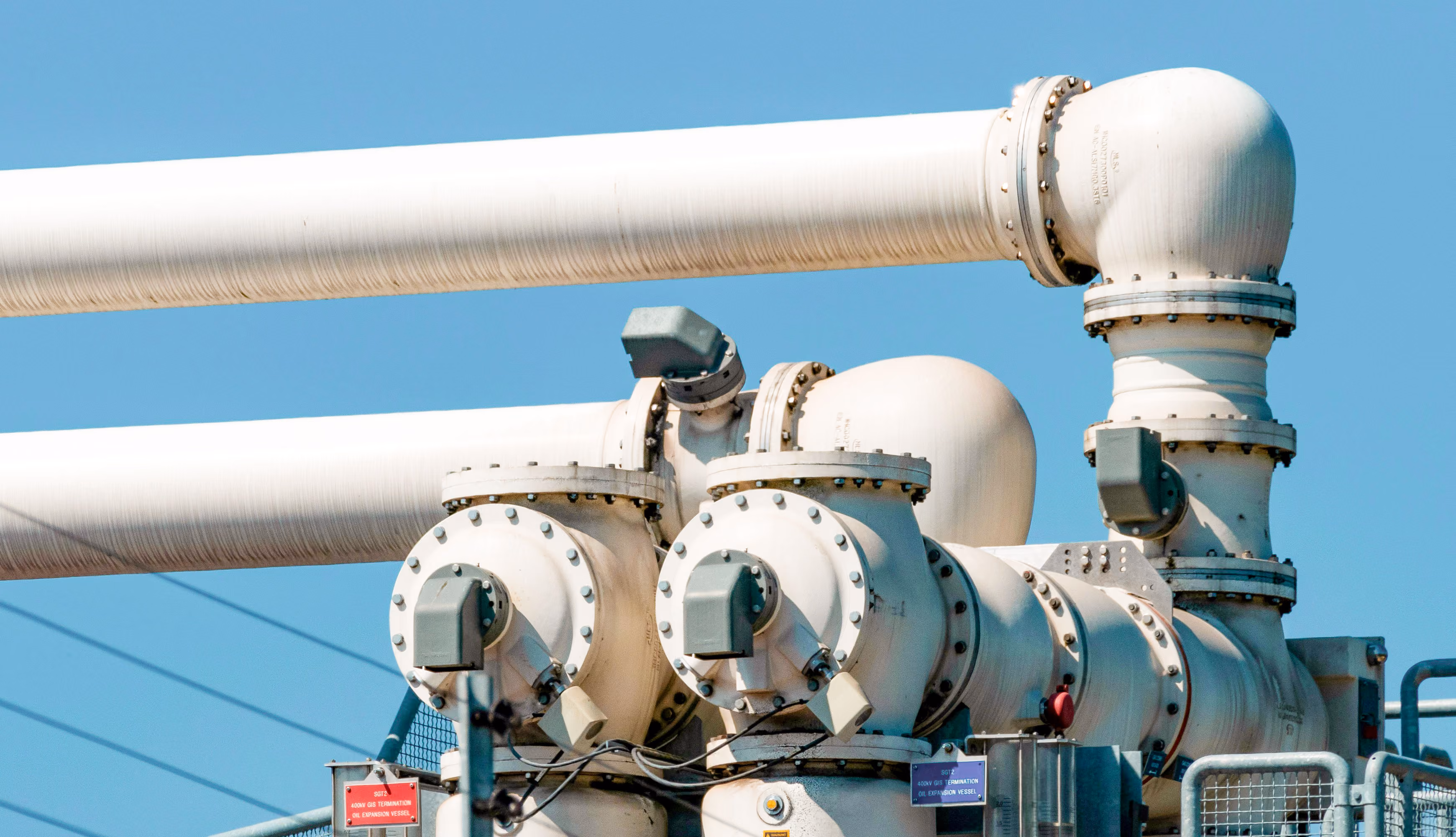 Close-up of white industrial pipes and valves with blue sky background.