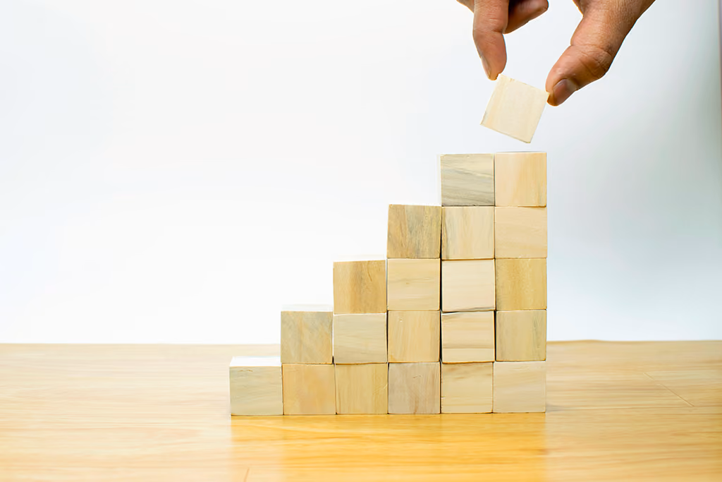 Une main empile un cube en bois sur une pyramide de cubes sur une table en bois.