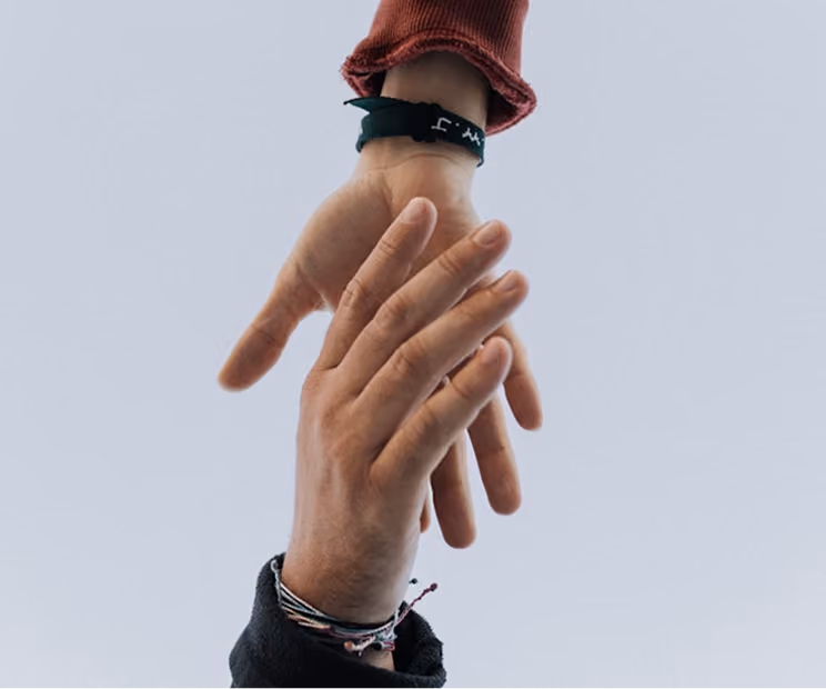Deux mains entrelacées, l'une portant un bracelet noir, l'autre plusieurs bracelets colorés.