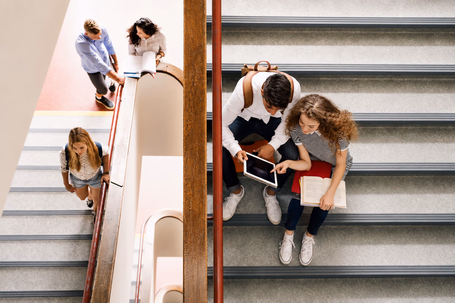 Deux étudiants assis sur les escaliers regardant une tablette tandis que deux autres discutent debout.