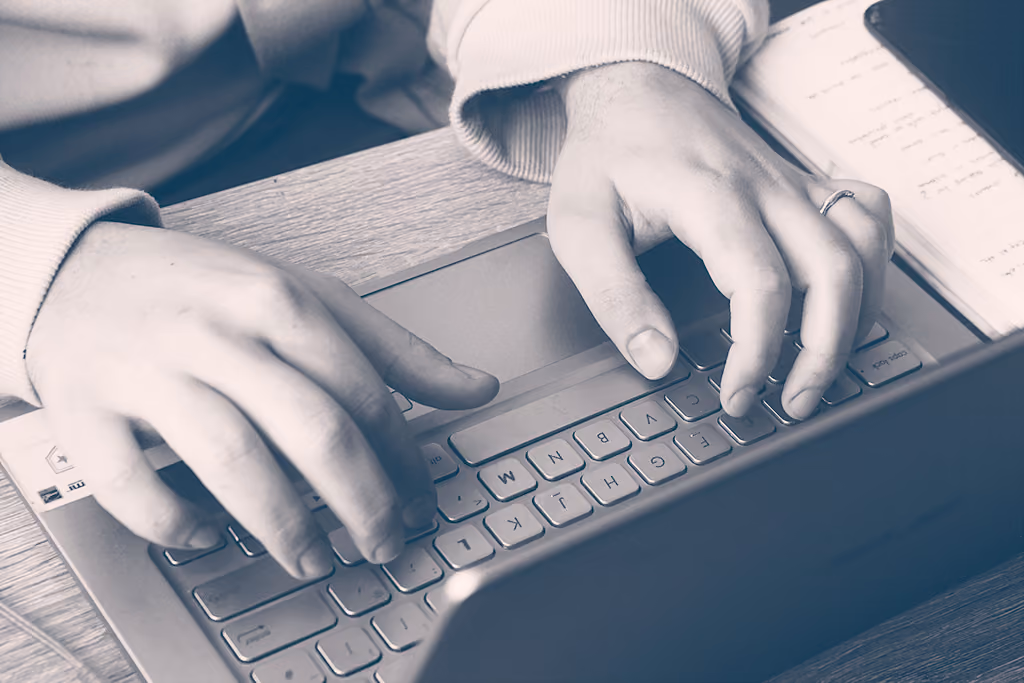 Mains d'une personne en train de taper sur un clavier d'ordinateur portable posé sur un bureau.
