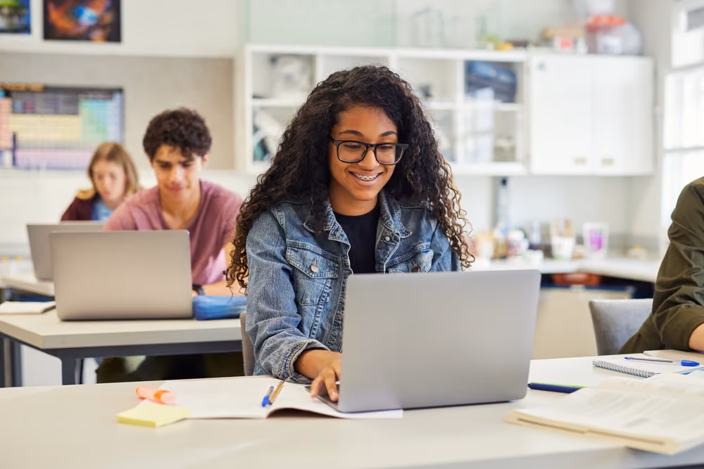 Students in a classroom working on laptops and studying with notebooks.