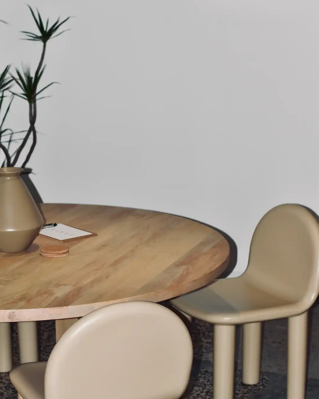 Corner of the Abōde studio with a round timber table, two curved sand-coloured chairs and a paper lantern.