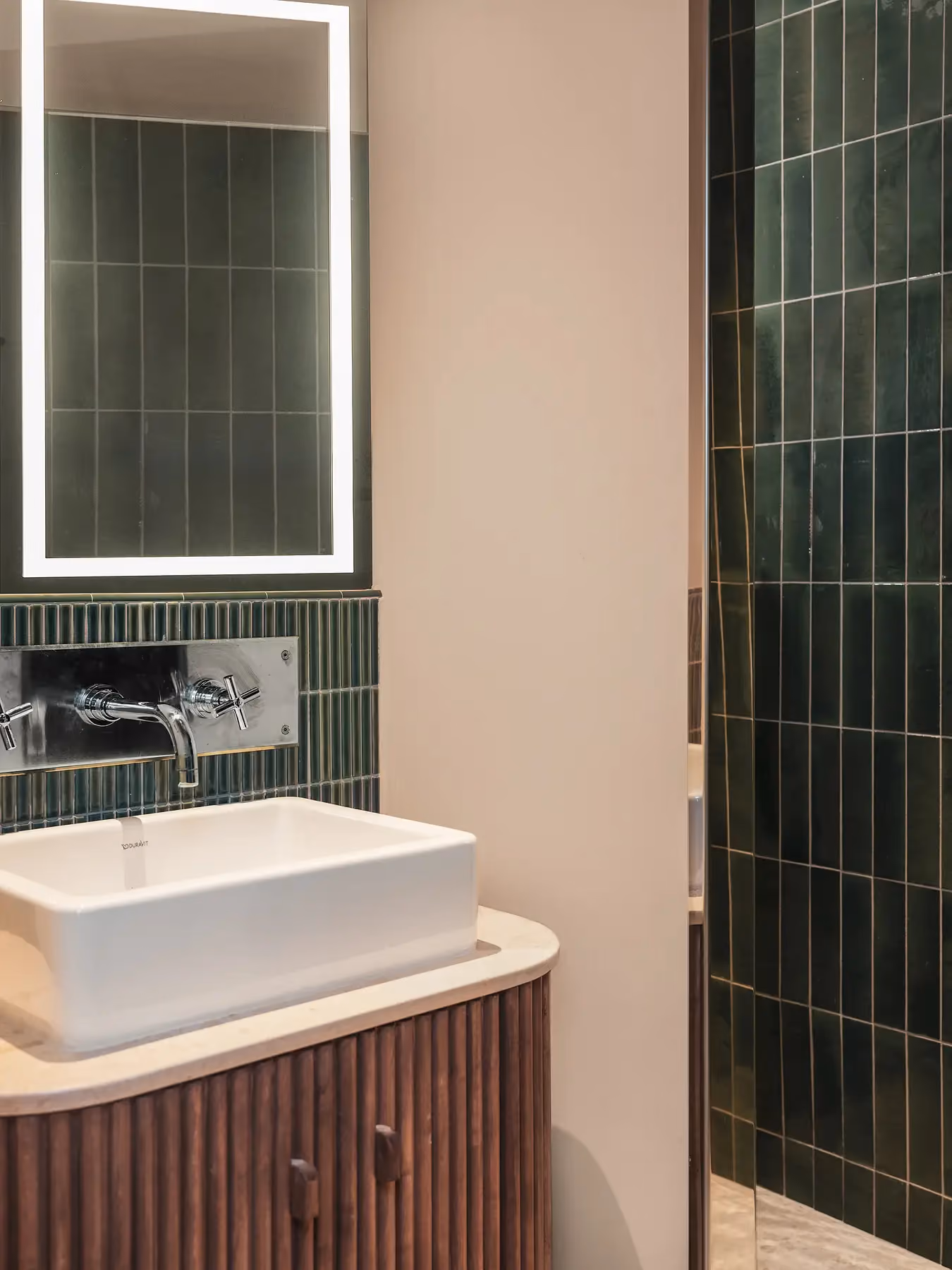 Salle de bain avec vasque posée, miroir lumineux et carreaux de douche vert foncé.