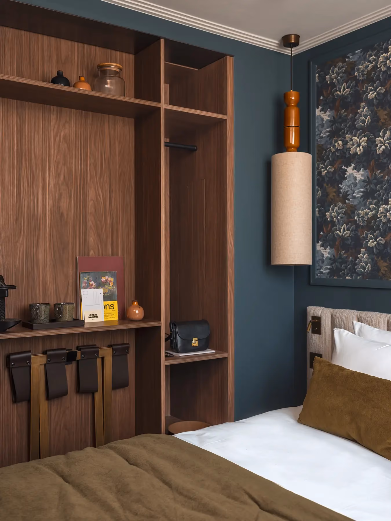 Coin rangement en bois avec cintres et étagère, chambre bleu marine au papier peint fleuri.