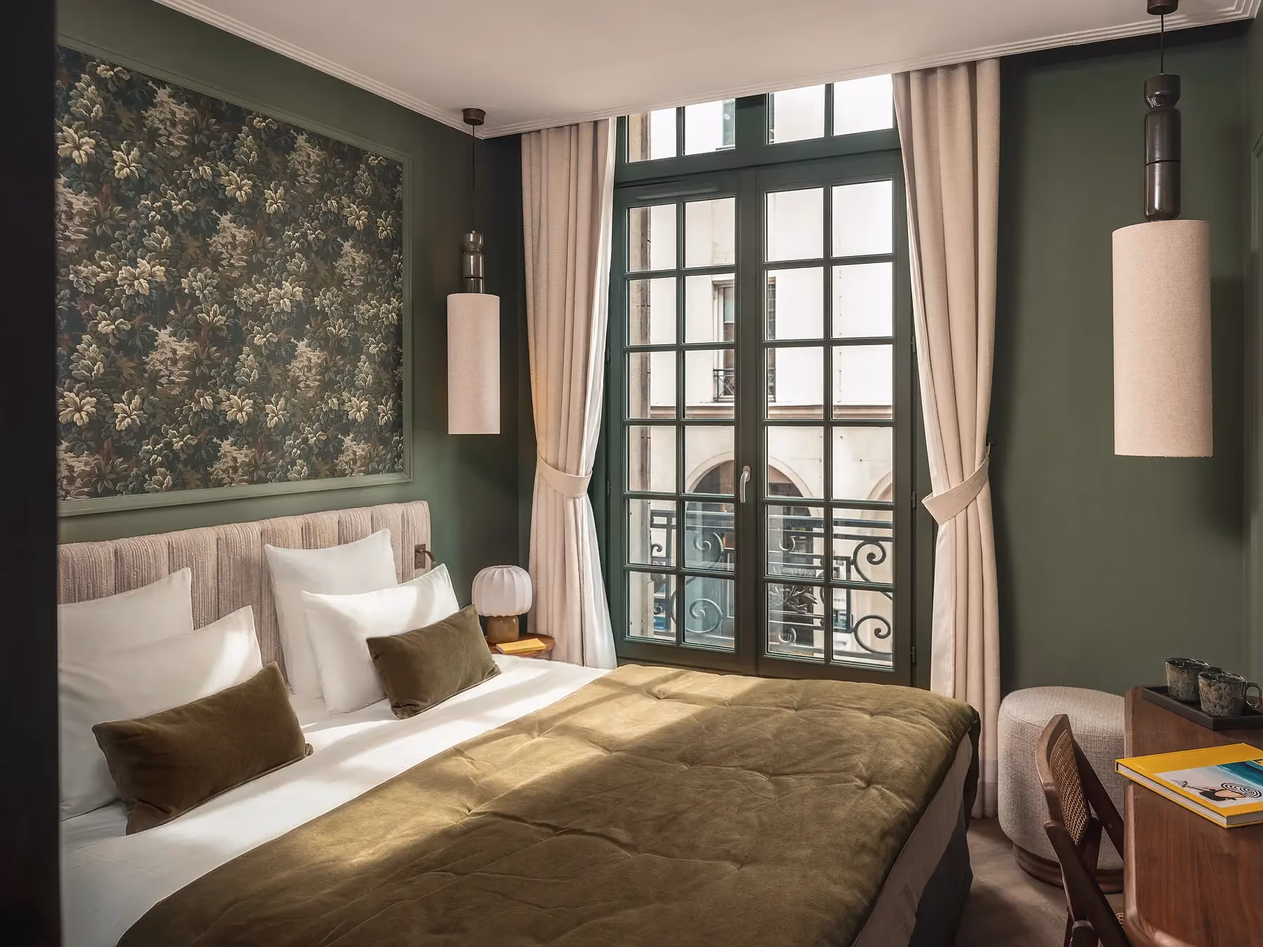 Chambre vert olive avec grande porte-fenêtre parisienne à balcon et tapisserie florale.