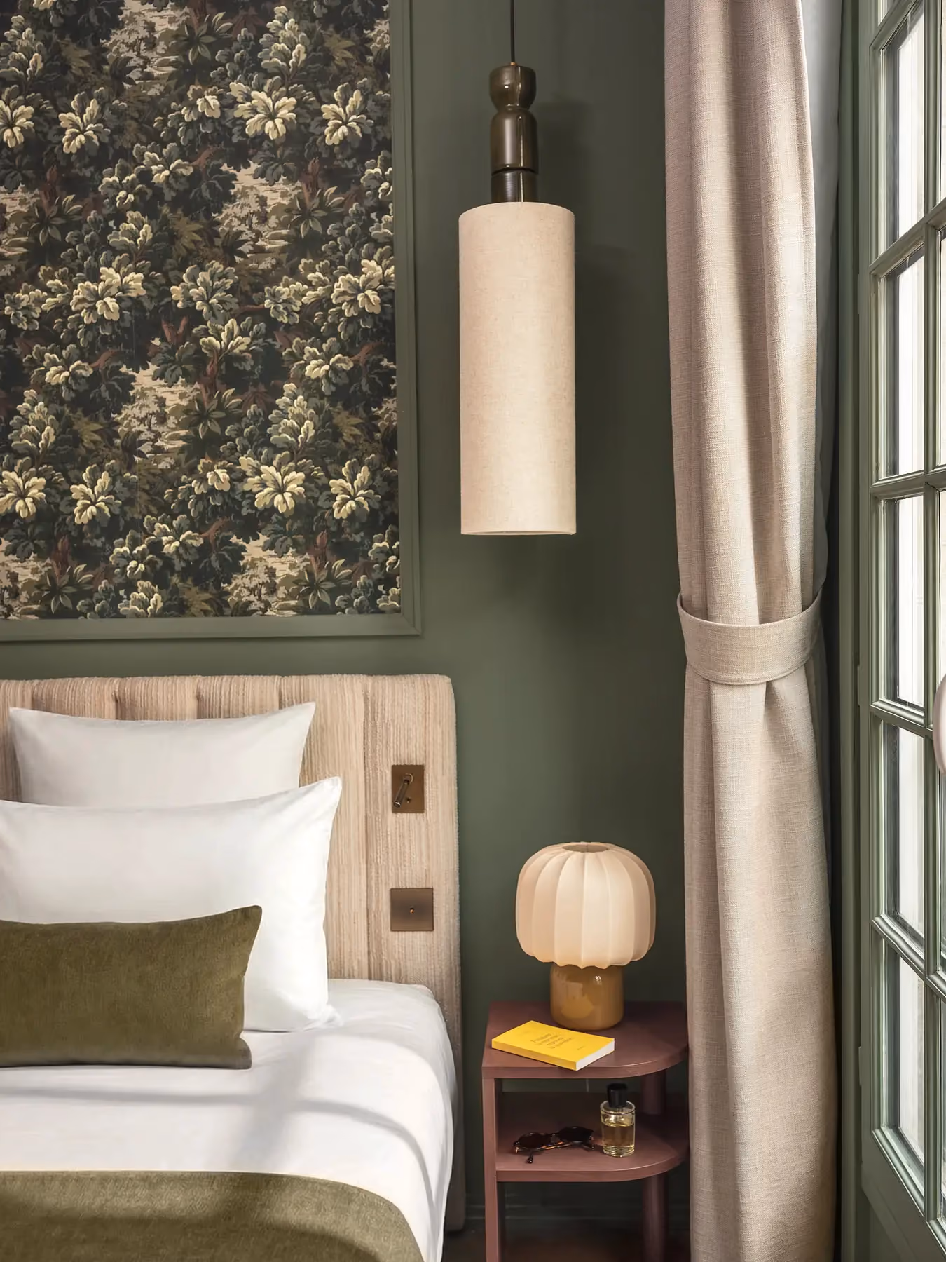 Coin chambre vert sauge avec table de chevet, lampe champignon et tapisserie florale.