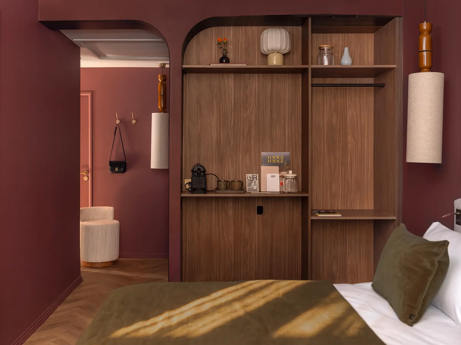 Chambre bordeaux avec meuble en bois arrondi et vue vers la salle de bain attenante.