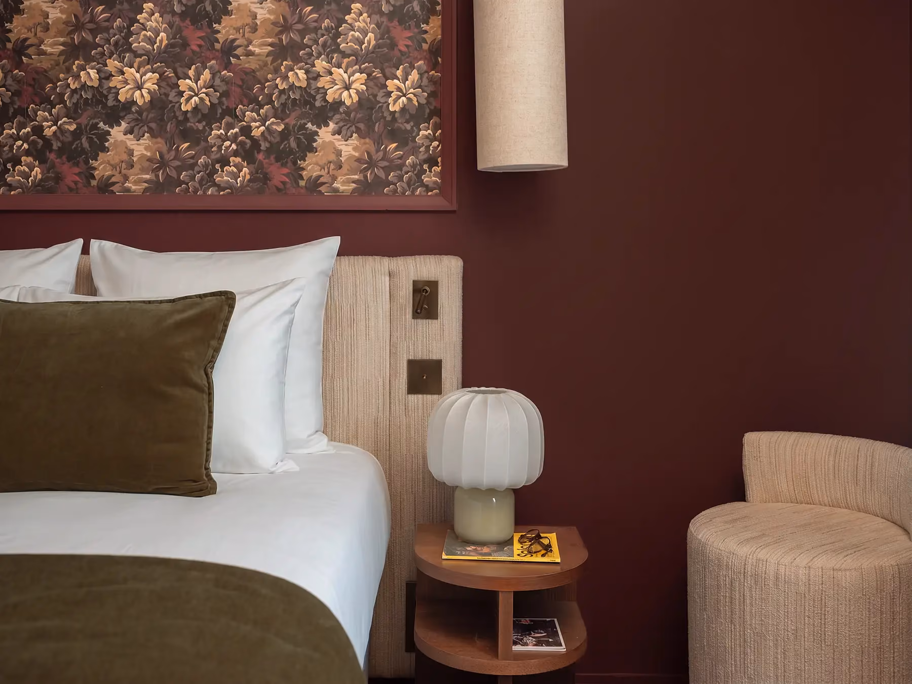 Coin chambre bordeaux avec table de chevet, lampe champignon et fauteuil en bouclé beige.