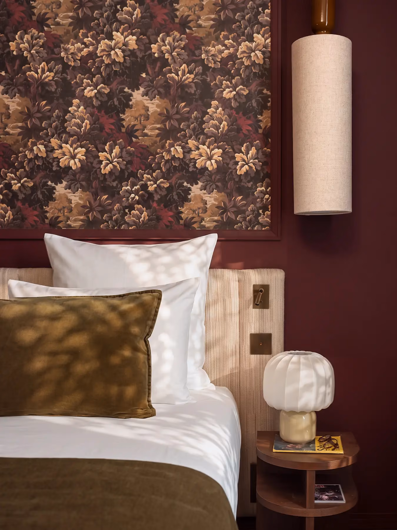 Détail d'une chambre bordeaux avec lampe champignon et suspension cylindrique près du lit.